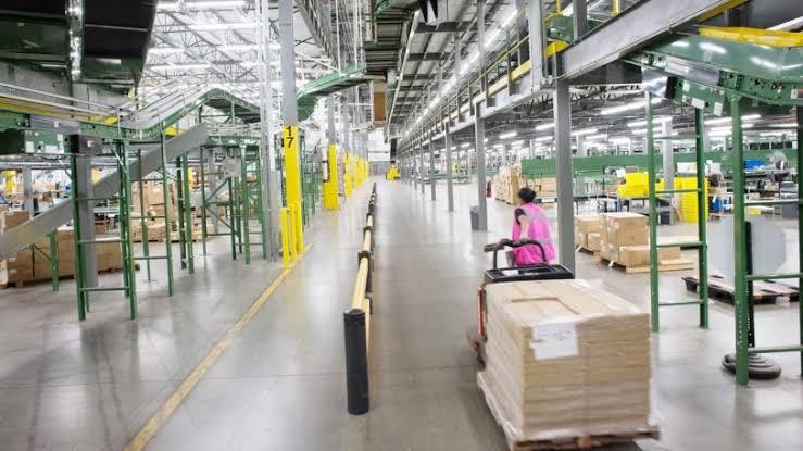 A warehouse worker moving a pallet of boxes with a hand truck down a warehouse aisle.